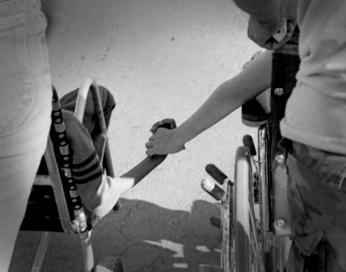 Holding Hands image from behind showing two kids in wheelchairs holding hands