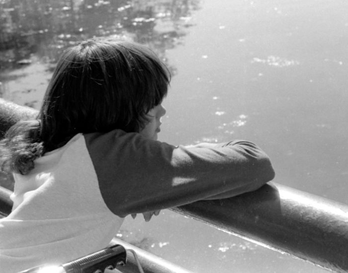 MDCamp looking over water A young girl in a wheelchair leaning on a railing looking wistfully across a lake.