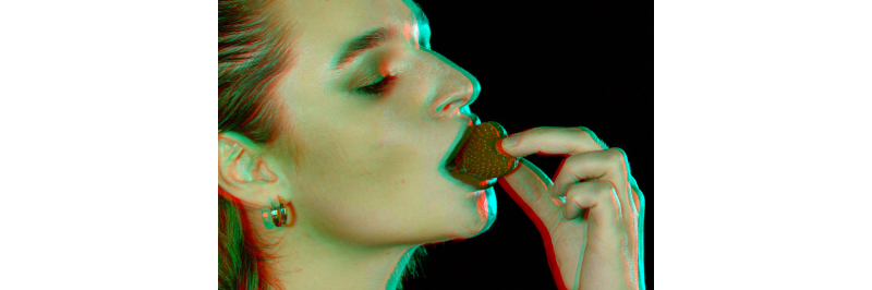 A stereo image of a profile of a beautiful young woman in red lipstick taking a bite out of a red strawberry