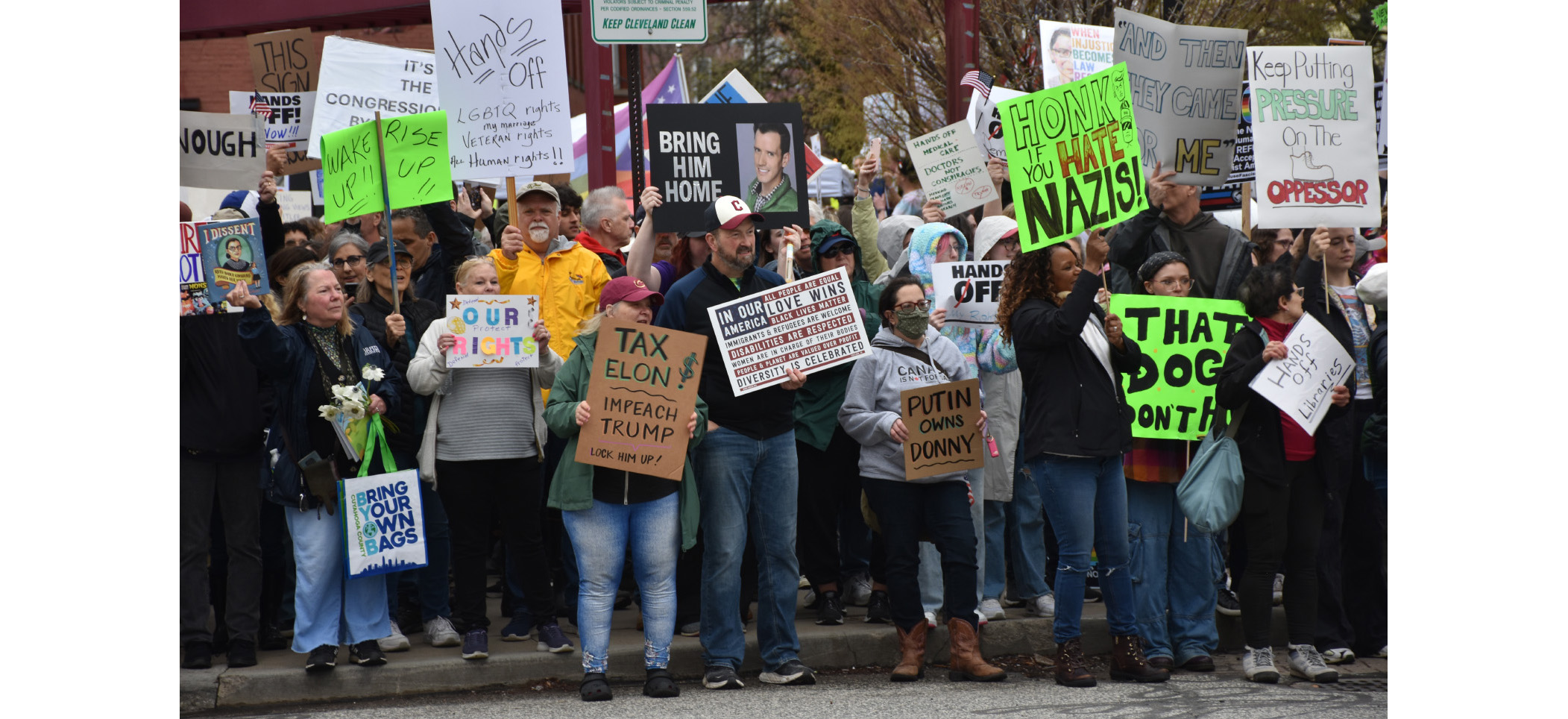 handsoff_protest Demonstrators at the 4/5/25 Hands Off Rally near the West Side Market in Cleveland, OH. This is a sampling of people lining the street holding signes saying: "That Doge Don't Hunt", "Honk if you Hate Nazis", "Wake Up, Wise Up", "Tax Elon, Deport Trump","Putin Owns Donny" and much more. The people are wearing hats and spring coats an standing on the curb. Demonstrators at the 4/5/25 Hands Off Rally near the West Side Market in Cleveland, OH. This is a sampling of people lining the street holding signes saying: "That Doge Don't Hunt", "Honk if you Hate Nazis", "Wake Up, Wise Up", "Tax Elon, Deport Trump","Putin Owns Donny" and much more. The people are wearing hats and spring coats an standing on the curb.