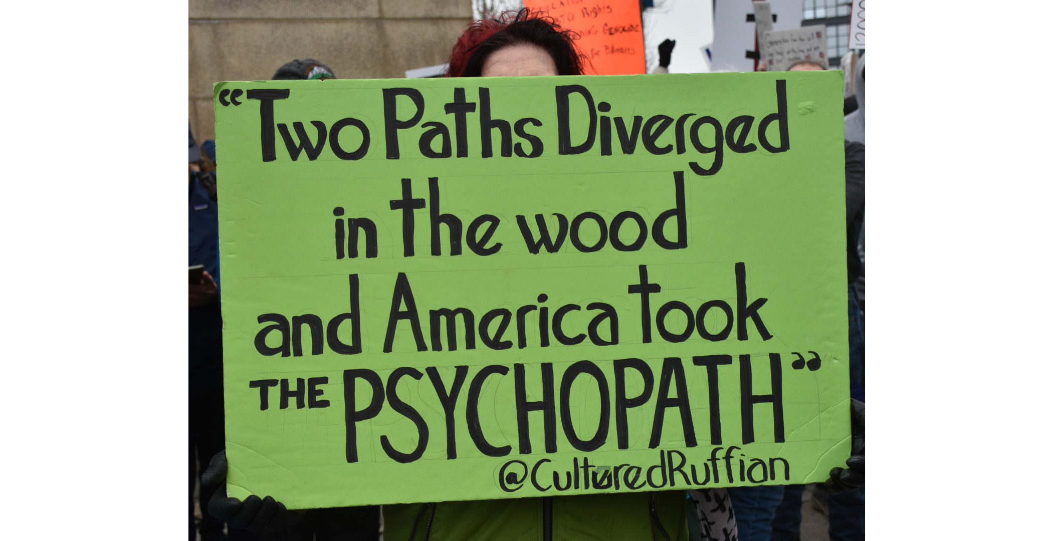 handsoff_protest3 A woman holding a green sign at the Cleveland Hands Off protest. All that is visible of the woman is her forehead and shortish red hair. The Sign says "Two Paths Diverged in the wood and America took the PSYCHOPATH @culturedRuffian A woman holding a green sign at the Cleveland Hands Off protest. All that is visible of the woman is her forehead and shortish red hair. The Sign says "Two Paths Diverged in the wood and America took the PSYCHOPATH @culturedRuffian