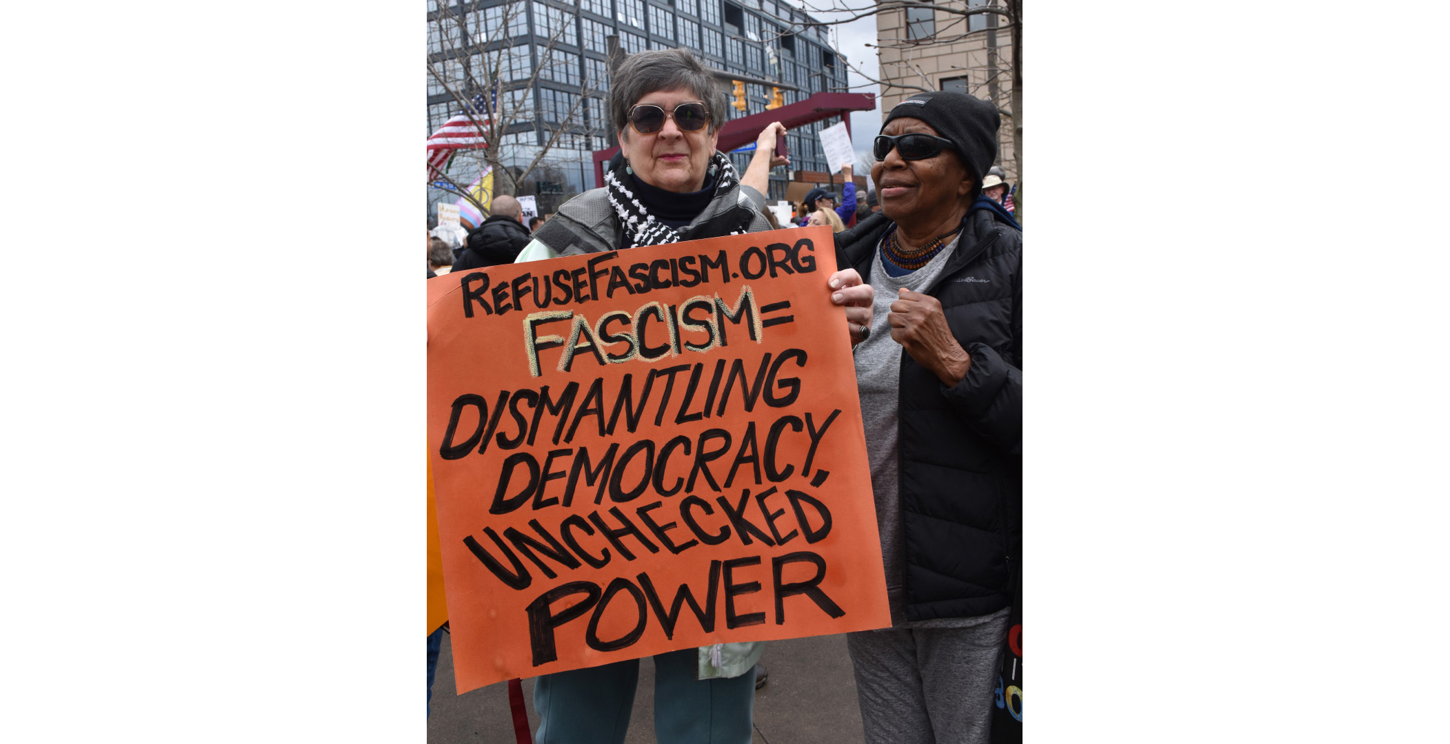 refusefascism Two woman sharing a sign that says "RefuseFascism.org; Fascism=Dismantling Democracy, Unchecked Power"